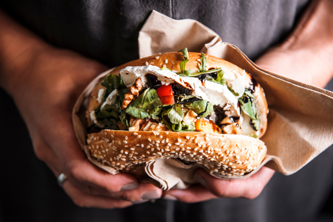 Woman is  holding a bagel fresh burger before eating.